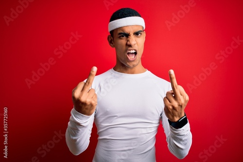 Young handsome african american sportsman wearing sportswear over red background Showing middle finger doing fuck you bad expression, provocation and rude attitude. Screaming excited