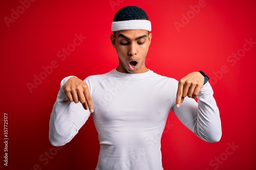 Young handsome african american sportsman wearing sportswear over red background Pointing down with fingers showing advertisement, surprised face and open mouth