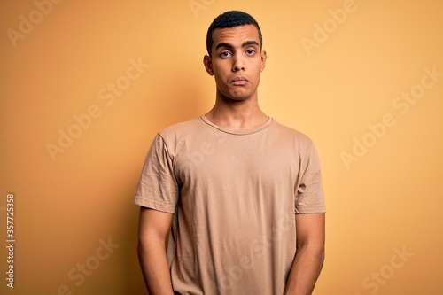 Young handsome african american man wearing casual t-shirt standing over yellow background Relaxed with serious expression on face. Simple and natural looking at the camera.