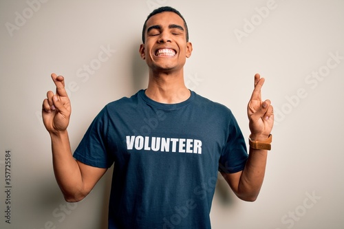 Young handsome african american man volunteering wearing t-shirt with volunteer message gesturing finger crossed smiling with hope and eyes closed. Luck and superstitious concept.