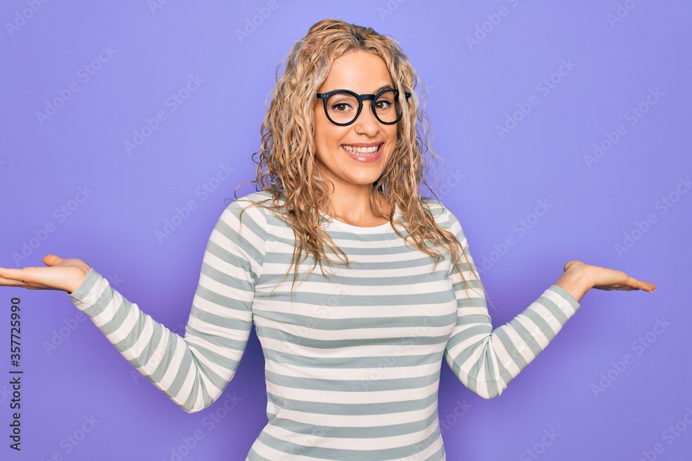 Beautiful blonde woman wearing casual striped t-shirt and glasses over purple background smiling showing both hands open palms, presenting and advertising comparison and balance Beautiful blonde woman wearing casual striped t-shirt and glasses over purple background smiling showing both hands open palms, presenting and advertising comparison and balance