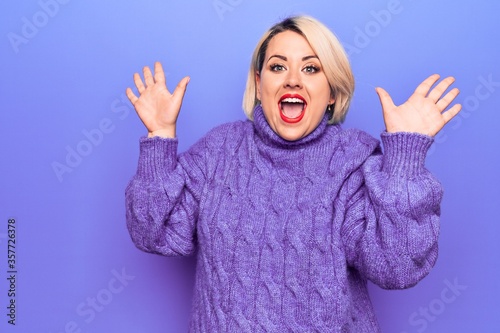 Beautiful blonde plus size woman wearing casual turtleneck sweater over purple background celebrating crazy and amazed for success with arms raised and open eyes screaming excited. Winner concept