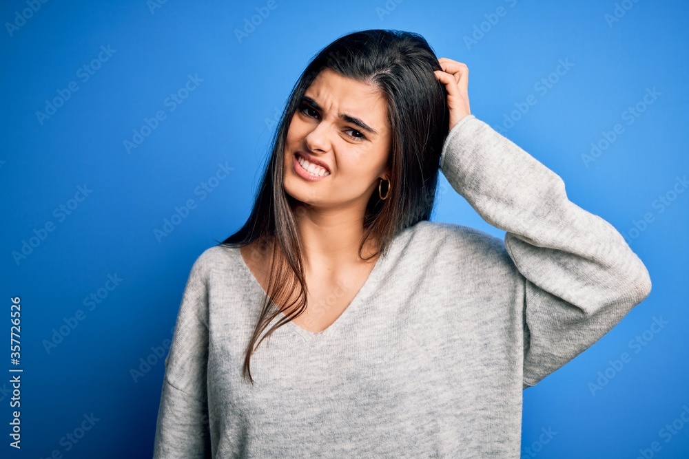 Fototapeta premium Young beautiful brunette woman wearing casual sweater standing over blue background confuse and wonder about question. Uncertain with doubt, thinking with hand on head. Pensive concept.