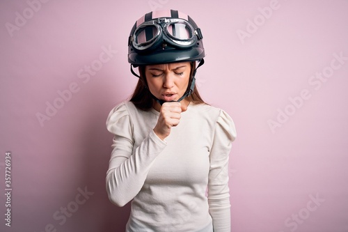 Young beautiful motorcyclist woman with blue eyes wearing moto helmet over pink background feeling unwell and coughing as symptom for cold or bronchitis. Health care concept.