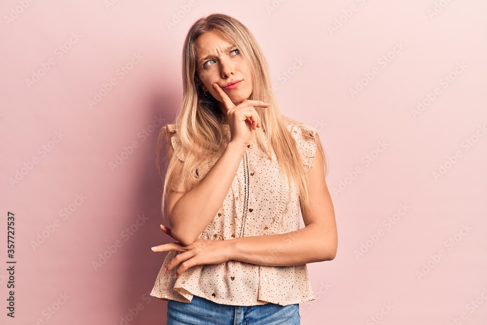Young blonde woman wearing casual clothes thinking concentrated about doubt with finger on chin and looking up wondering Young blonde woman wearing casual clothes thinking concentrated about doubt with finger on chin and looking up wondering