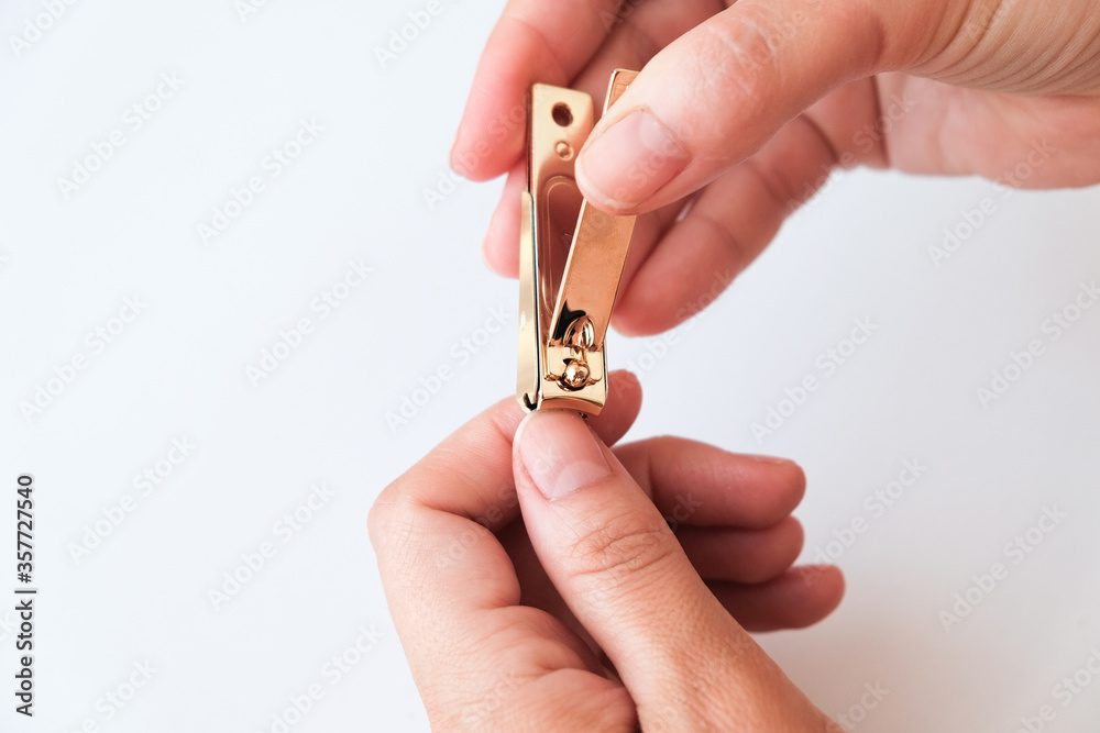 Woman hands using a nail clippers to cut her fingernails on a white background. View from above. Manicure at home