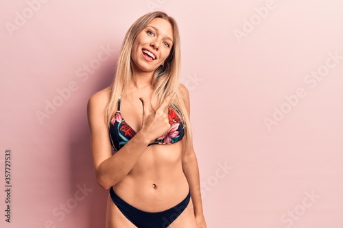 Young beautiful blonde woman wearing bikini smiling cheerful pointing with hand and finger up to the side © Krakenimages.com