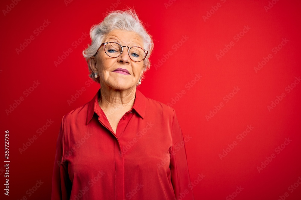 Senior beautiful grey-haired woman wearing casual shirt and glasses over red background Relaxed with serious expression on face. Simple and natural looking at the camera. Senior beautiful grey-haired woman wearing casual shirt and glasses over red background Relaxed with serious expression on face. Simple and natural looking at the camera.