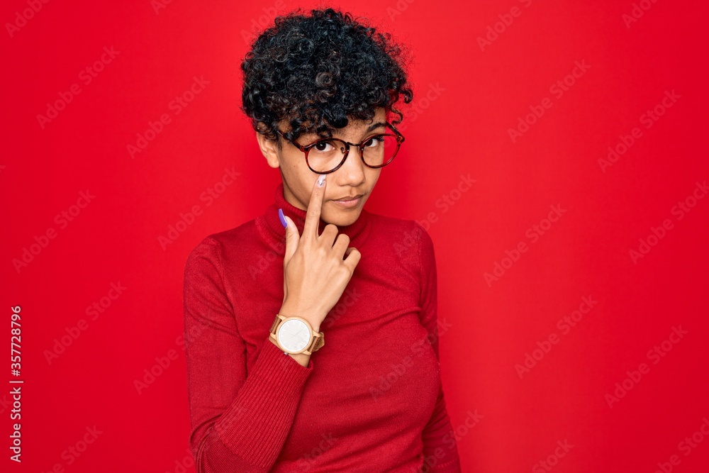 Young beautiful african american afro woman wearing turtleneck sweater and glasses Pointing to the eye watching you gesture, suspicious expression Young beautiful african american afro woman wearing turtleneck sweater and glasses Pointing to the eye watching you gesture, suspicious expression