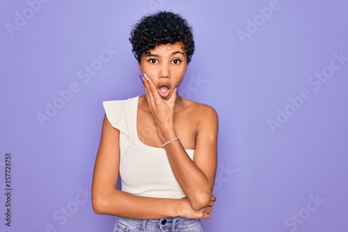 Young beautiful african american afro woman wearing casual t-shirt over purple background Looking fascinated with disbelief, surprise and amazed expression with hands on chin