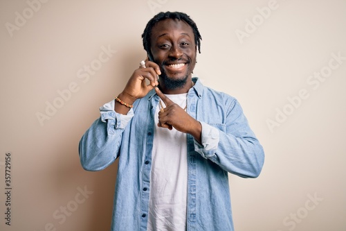 African american man having conversation talking on the smartphone over white background very happy pointing with hand and finger photo