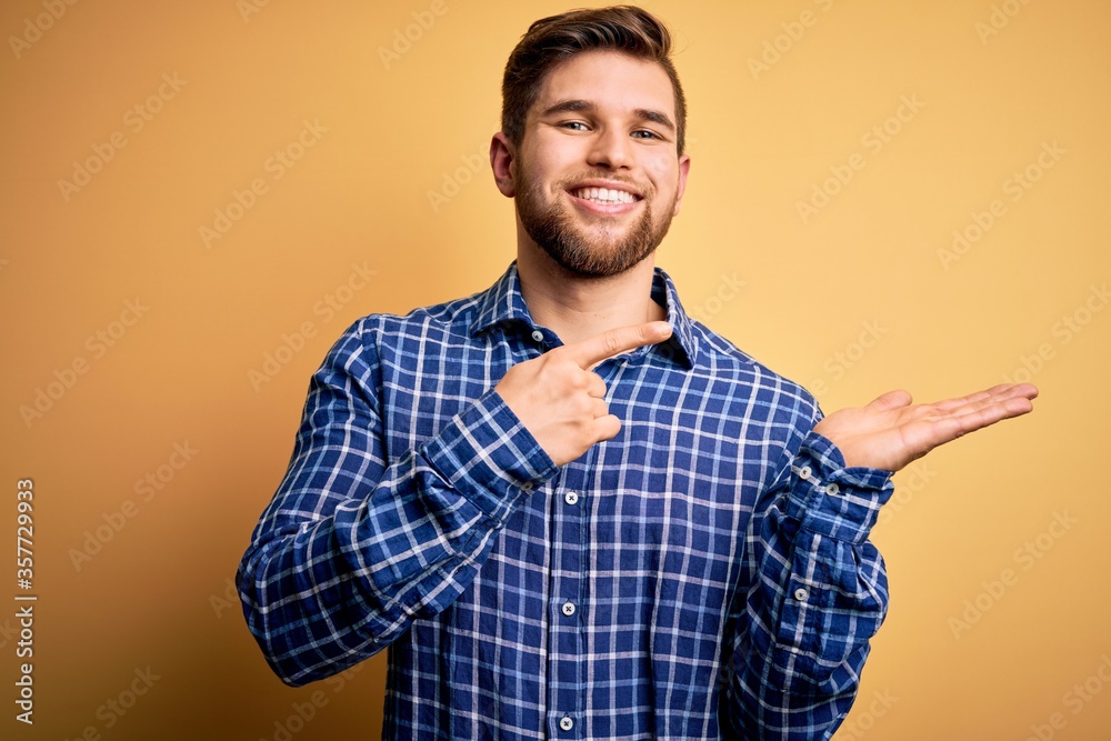 Young blond businessman with beard and blue eyes wearing shirt over yellow background amazed and smiling to the camera while presenting with hand and pointing with finger. Young blond businessman with beard and blue eyes wearing shirt over yellow background amazed and smiling to the camera while presenting with hand and pointing with finger.