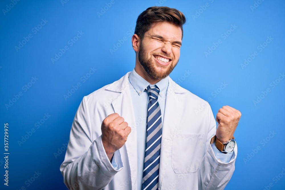 Young blond therapist man with beard and blue eyes wearing coat and tie over background excited for success with arms raised and eyes closed celebrating victory smiling. Winner concept.