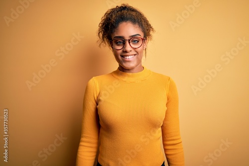 Young beautiful african american girl wearing sweater and glasses over yellow background with a happy and cool smile on face. Lucky person. © Krakenimages.com