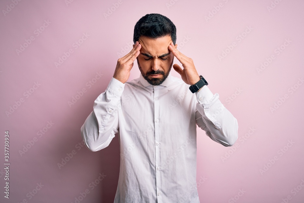 Young handsome man with beard wearing casual shirt standing over pink background with hand on head for pain in head because stress. Suffering migraine. Young handsome man with beard wearing casual shirt standing over pink background with hand on head for pain in head because stress. Suffering migraine.