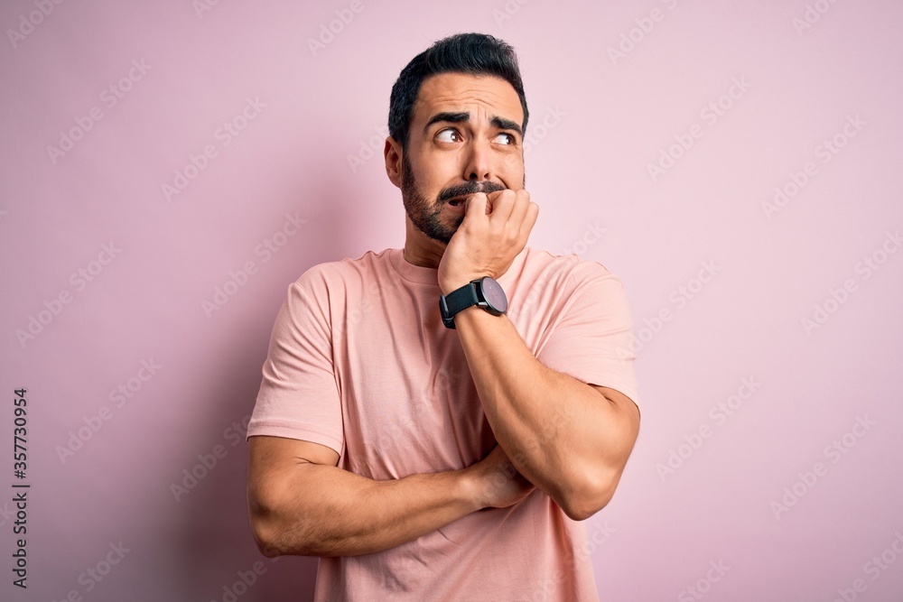 Young handsome man with beard wearing casual t-shirt standing over pink background looking stressed and nervous with hands on mouth biting nails. Anxiety problem. Young handsome man with beard wearing casual t-shirt standing over pink background looking stressed and nervous with hands on mouth biting nails. Anxiety problem.