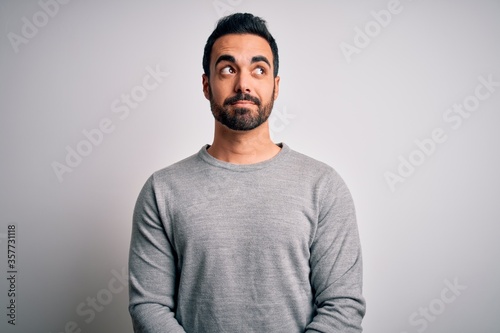 Young handsome man with beard wearing casual sweater standing over white background smiling looking to the side and staring away thinking.