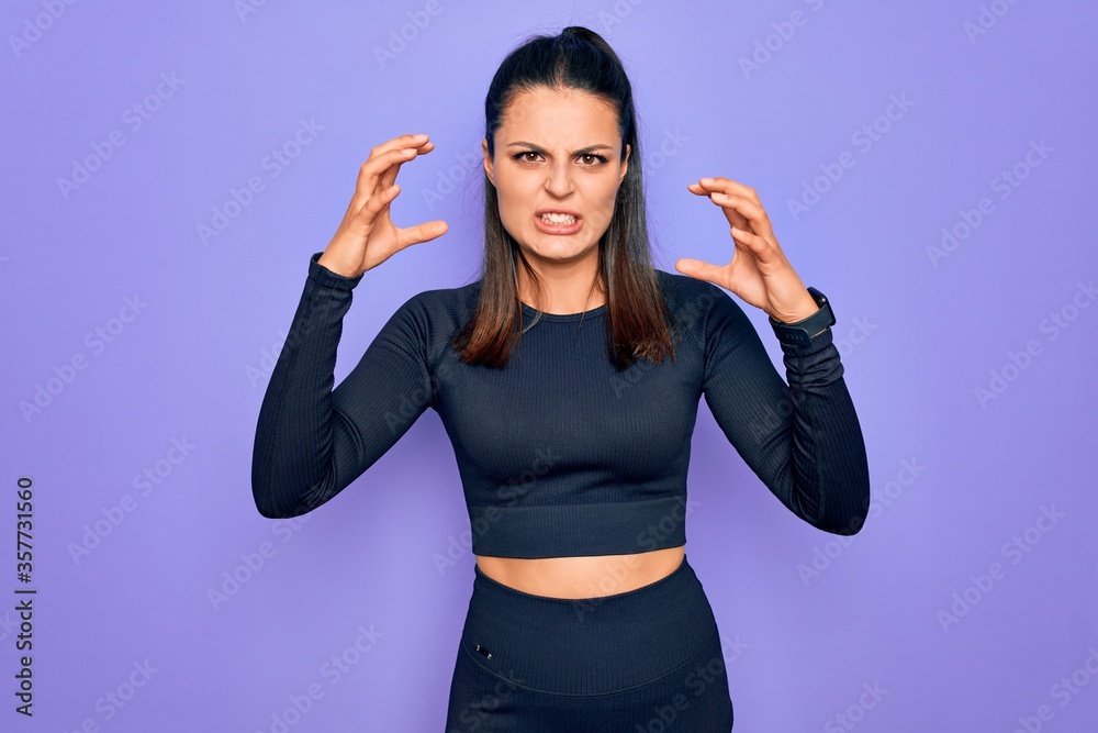 Fototapeta premium Young beautiful brunette sporty woman wearing casual sportswear over purple background Shouting frustrated with rage, hands trying to strangle, yelling mad