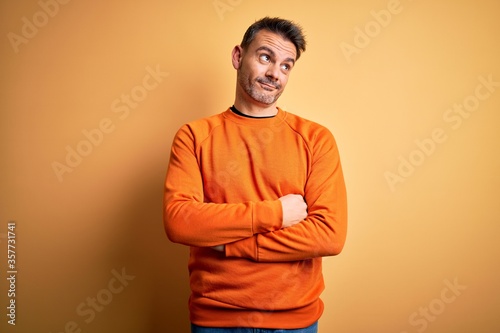 Young handsome man wearing orange casual sweater standing over isolated yellow background smiling looking to the side and staring away thinking.