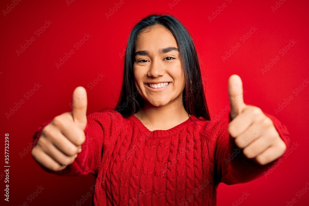 Young beautiful asian woman wearing casual sweater standing over isolated red background approving doing positive gesture with hand, thumbs up smiling and happy for success. Winner gesture. Young beautiful asian woman wearing casual sweater standing over isolated red background approving doing positive gesture with hand, thumbs up smiling and happy for success. Winner gesture.