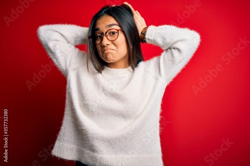 Young beautiful asian woman wearing casual sweater and glasses over red background Doing bunny ears gesture with hands palms looking cynical and skeptical. Easter rabbit concept. © Krakenimages.com