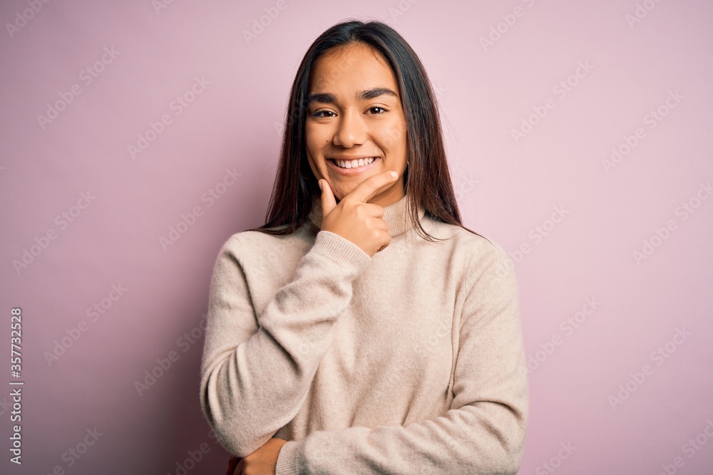 Young beautiful asian woman wearing casual turtleneck sweater over pink background looking confident at the camera smiling with crossed arms and hand raised on chin. Thinking positive. Young beautiful asian woman wearing casual turtleneck sweater over pink background looking confident at the camera smiling with crossed arms and hand raised on chin. Thinking positive.