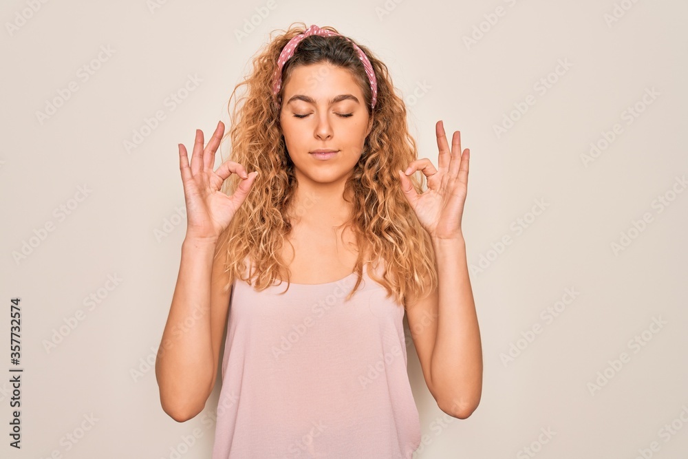 Young beautiful woman with blue eyes wearing casual t-shirt and diadem over pink background relax and smiling with eyes closed doing meditation gesture with fingers. Yoga concept.