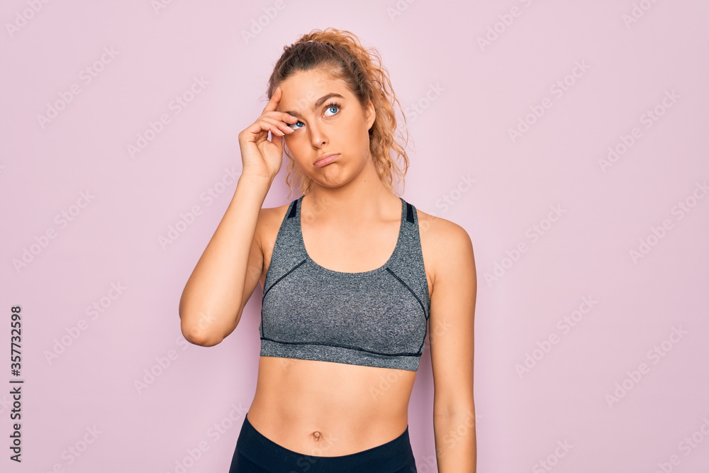 Young beautiful blonde sportswoman with blue eyes doing exercise wearing sportswear worried and stressed about a problem with hand on forehead, nervous and anxious for crisis
