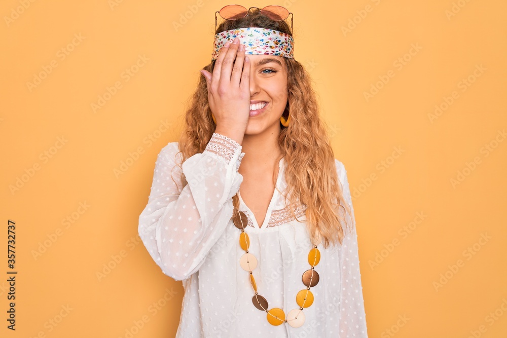 Young beautiful blonde hippie woman with blue eyes wearing sunglasses and accessories covering one eye with hand, confident smile on face and surprise emotion. Young beautiful blonde hippie woman with blue eyes wearing sunglasses and accessories covering one eye with hand, confident smile on face and surprise emotion.