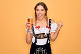 Beautiful blonde german woman with blue eyes wearing octoberfest dress drinking glass of beer screaming proud and celebrating victory and success very excited, cheering emotion