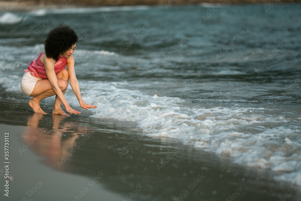 Mixed-race woman kneeling the edge of the surf on the tropical sea beach.