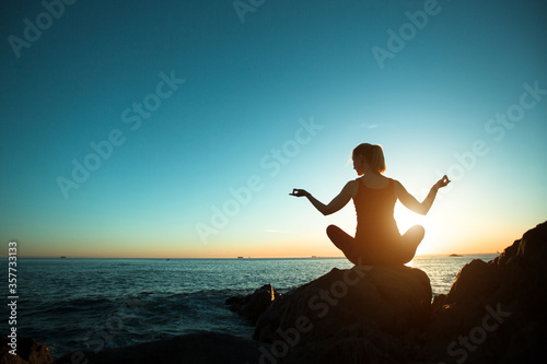 Silhouette young woman practicing yoga during surreal sunset on the beach.