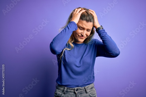 Young beautiful blonde woman wearing casual t-shirt over isolated purple background suffering from headache desperate and stressed because pain and migraine. Hands on head.