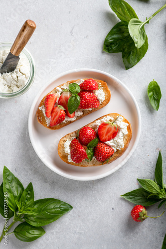 bruschettas with strawberries, cream cheese and basil in a white plate on a light background, top view