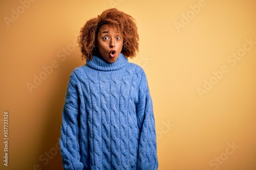 Young beautiful African American afro woman with curly hair wearing blue turtleneck sweater afraid and shocked with surprise expression, fear and excited face.