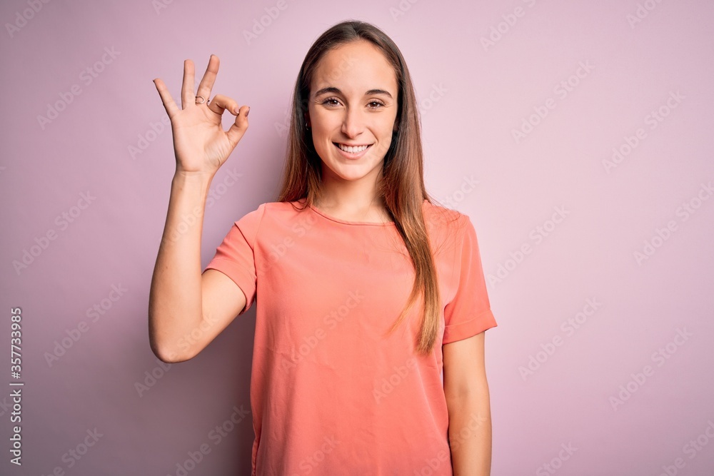 Young beautiful woman wearing casual t-shirt standing over isolated pink background smiling positive doing ok sign with hand and fingers. Successful expression. Young beautiful woman wearing casual t-shirt standing over isolated pink background smiling positive doing ok sign with hand and fingers. Successful expression.