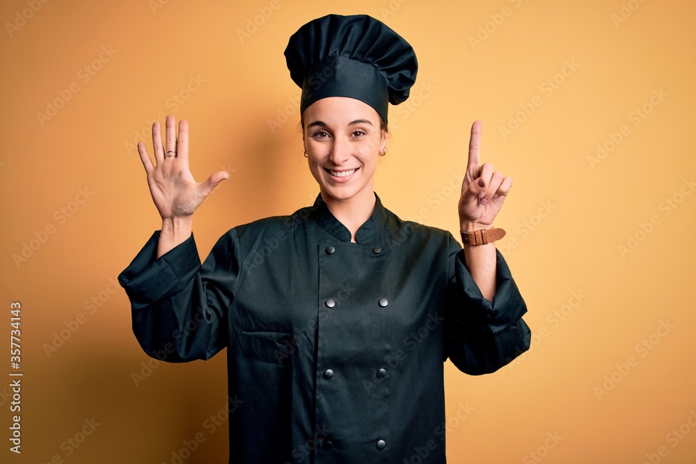 Young beautiful chef woman wearing cooker uniform and hat standing over yellow background showing and pointing up with fingers number six while smiling confident and happy. Young beautiful chef woman wearing cooker uniform and hat standing over yellow background showing and pointing up with fingers number six while smiling confident and happy.