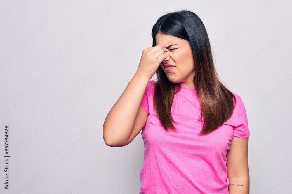 Young beautiful brunette woman wearing casual pink t-shirt standing over white background tired rubbing nose and eyes feeling fatigue and headache. Stress and frustration concept. Young beautiful brunette woman wearing casual pink t-shirt standing over white background tired rubbing nose and eyes feeling fatigue and headache. Stress and frustration concept.