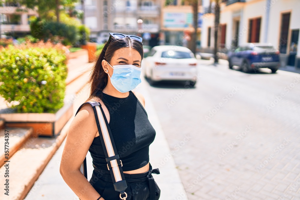 Fototapeta premium Young beautiful brunette woman wearing medical mask. Walking at town street