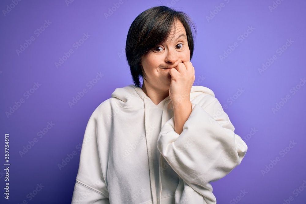 Young down syndrome sports woman wearing fitness sweatshirt over purple background looking stressed and nervous with hands on mouth biting nails. Anxiety problem. Young down syndrome sports woman wearing fitness sweatshirt over purple background looking stressed and nervous with hands on mouth biting nails. Anxiety problem.