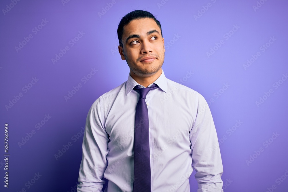 Young brazilian businessman wearing elegant tie standing over isolated purple background smiling looking to the side and staring away thinking. Young brazilian businessman wearing elegant tie standing over isolated purple background smiling looking to the side and staring away thinking.