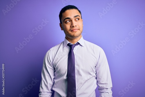 Young brazilian businessman wearing elegant tie standing over isolated purple background smiling looking to the side and staring away thinking. © Krakenimages.com