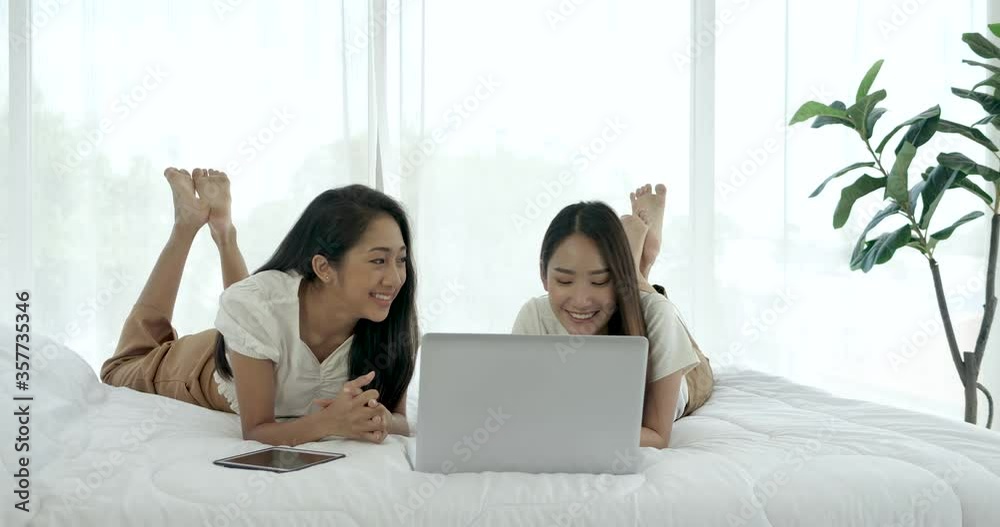 Smiling friend girls shopping online in a bedroom Smiling friend girls shopping online in a bedroom