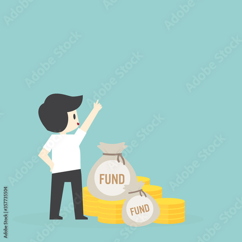 Young businessman In a white shirt with self-confidence Standing beside the pile of money and using his hand to point to the highest point he wants to reach Which represents the prosperous economic 