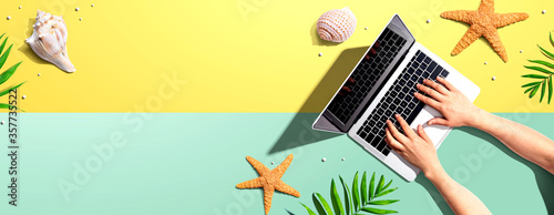 Person using a laptop computer with summer theme objects - flat lay