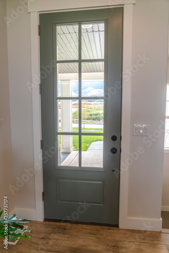 Front door with balck knob and glass panes against white wall and wood floor