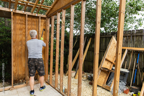 Foto Demolition phase with a man tearing down an old shed with a crowbar in a backyar
