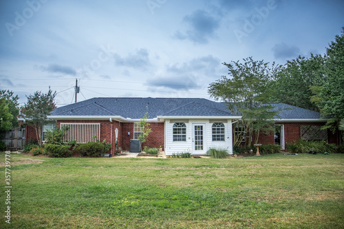 The rear view of a 1980's style red brick ranch house with white siding and a large backyard