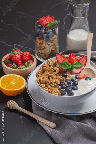 Bowl of homemade granola yogurt with fresh berries, strawberry, orange and milk on black table for breakfast