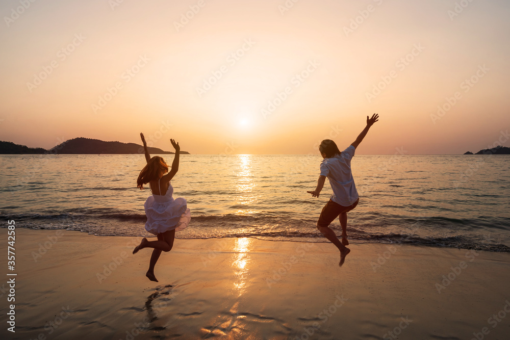 Young couple jumping on the beach at beautiful sunset, Couple on vacation in summer concept